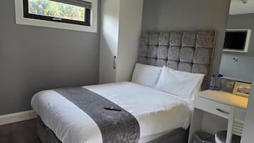 Un dormitorio con cama, cabecera, ventana, armario, escritorio y cubo de basura.
