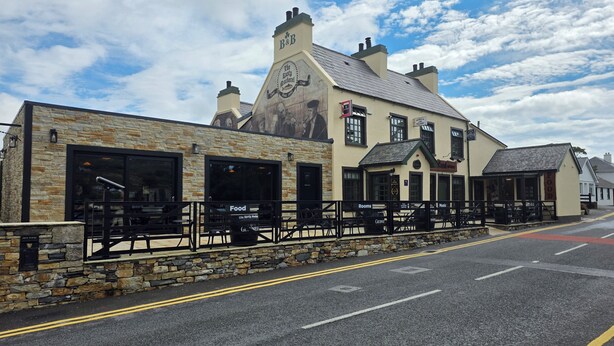 A building with a stone facade, multiple windows, and outdoor seating areas. - The rusty Mackerel  (DL)
