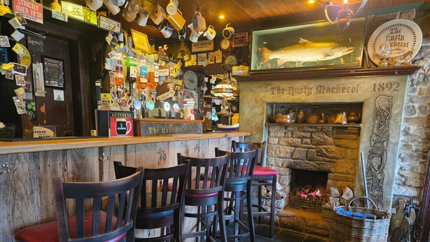 A bar area with a stone fireplace, wooden bar counter, and multiple stools.