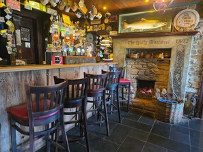Zona de bar con chimenea de piedra, mostrador de bar de madera y varios taburetes.