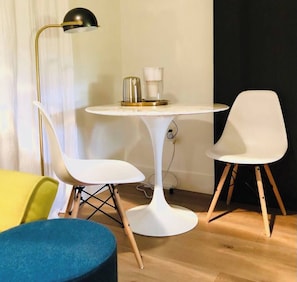 A modern room with a round white table, two white chairs, a yellow sofa, and a blue ottoman.