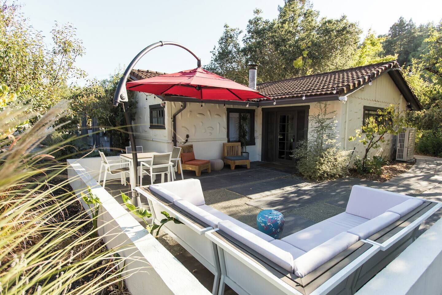 Un patio con mobiliario exterior, un paraguas rojo y un edificio con techo de tejas.