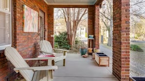 A covered porch with brick walls, two white Adirondack chairs, a table, and a potted plant. - Serene Nashville Executive and Family Retreat Minutes to 12 South & Green Hills (Nashville)