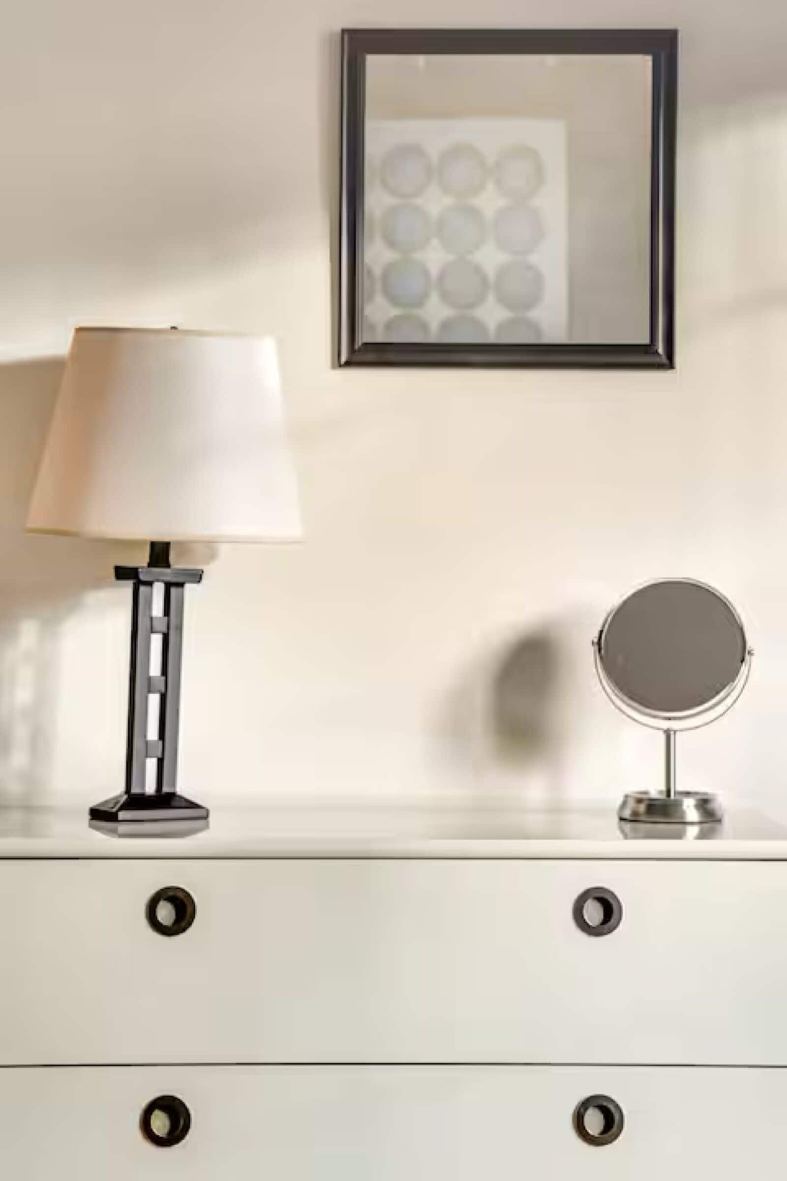Et natbord med en lampe, et spejl og et billede i ramme på væggen.