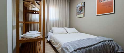 A hotel room with a bed, a wooden wardrobe with hanging clothes, a poster on the wall, and an air conditioning unit.