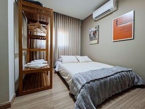 Ein Hotelzimmer mit einem Bett, einem Holzschrank mit Kleidung und einem Poster an der Wand, sowie einer Klimaanlage.