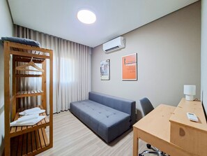 A hotel room with a bed, a wooden wardrobe, a desk, and a wall-mounted air conditioner. - Apto c Garagem Piscina e Sauna no Savassi (Belo Horizonte)
