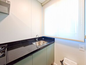 A kitchen with a black countertop, stainless steel sink, and light green cabinets. - Apto c Garagem Piscina e Sauna no Savassi (Belo Horizonte)