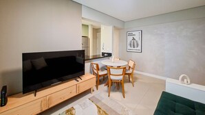 Un salon moderne doté d’un téléviseur à écran plat, de meubles en bois, d’un coin repas avec une table ronde et d’une cuisine en arrière-plan.