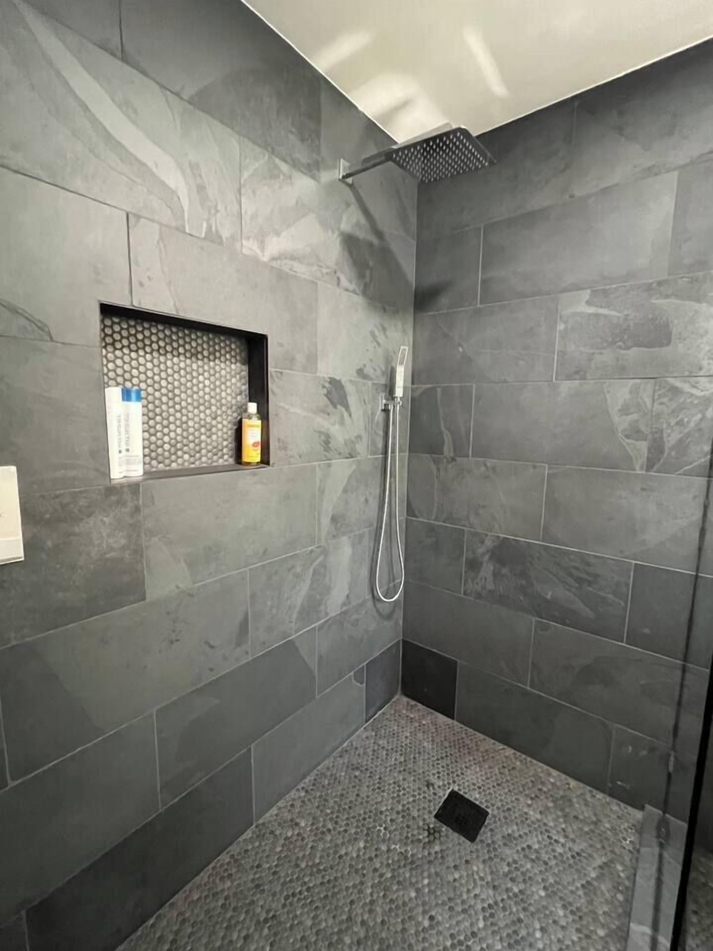 Ducha con cabezal de ducha de mano y zona de ducha con mampara de vidrio.