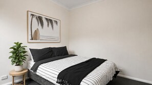 Un dormitorio con una cama, una planta en maceta y un cuadro en la pared.