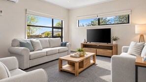A modern living room with a sofa, coffee table, TV, and windows with a view of trees. - Seamist Retreat - A relaxing coastal escape designed for easy holiday living (Indented Head)