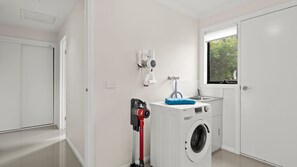 A laundry room with a washing machine, a dryer, a water heater, and a window with a view of trees. - Seamist Retreat - A relaxing coastal escape designed for easy holiday living (Indented Head)