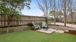 A backyard with artificial grass, two green chairs, a fire pit, and a wooden fence.