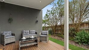 An outdoor patio with wicker furniture and a table, surrounded by a wooden deck and a grassy area. - Seamist Retreat - A relaxing coastal escape designed for easy holiday living (Indented Head)