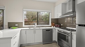 A modern kitchen with a built-in dishwasher, stainless steel appliances, and a window overlooking a backyard.