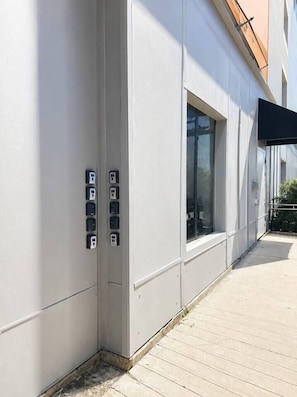 A building exterior with a modern design, featuring a large window and a series of electrical boxes on the wall.