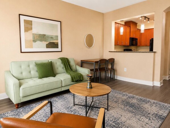 A living room with a sofa, coffee table, and chairs, a dining area with a table and chairs, and a kitchen with wooden cabinets and appliances.