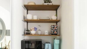 A compact kitchen with built-in appliances, shelves with decorative items, and a microwave.