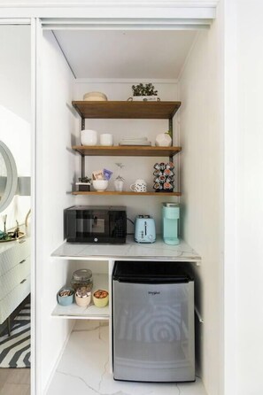 A compact kitchen with built-in appliances, shelves with decorative items, and a microwave.