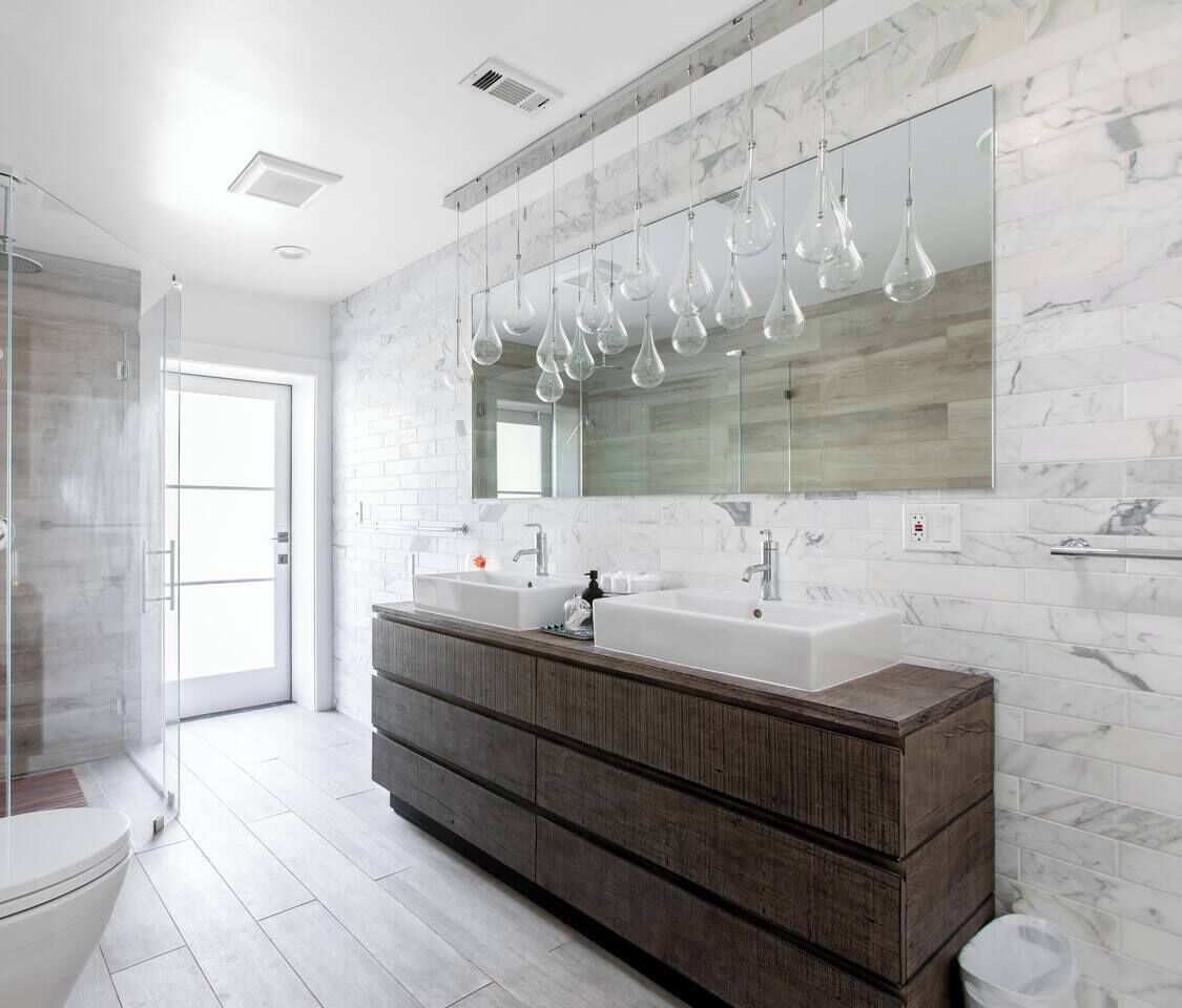 Un baño moderno con tocador doble, cabina de ducha de vidrio y un espejo grande con lámparas colgantes.