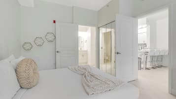 A modern bedroom with a large bed, a bathroom visible through an open door, and a kitchenette area.