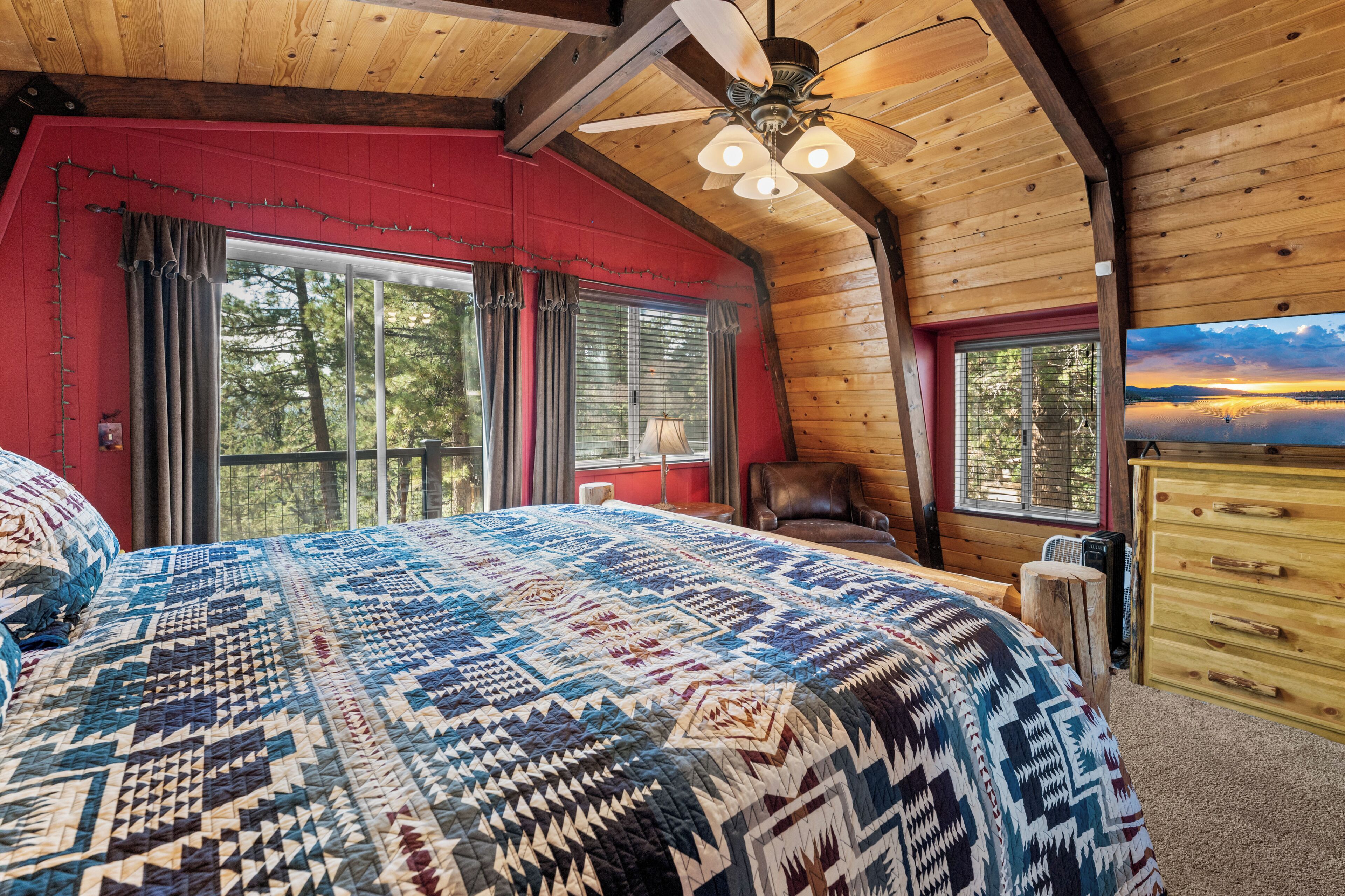 Une chambre avec un grand lit, un ventilateur de plafond en bois et une vue sur l’extérieur.