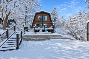 Una cabaña con una escalera pronunciada que lleva a un porche, rodeada de árboles cubiertos de nieve.