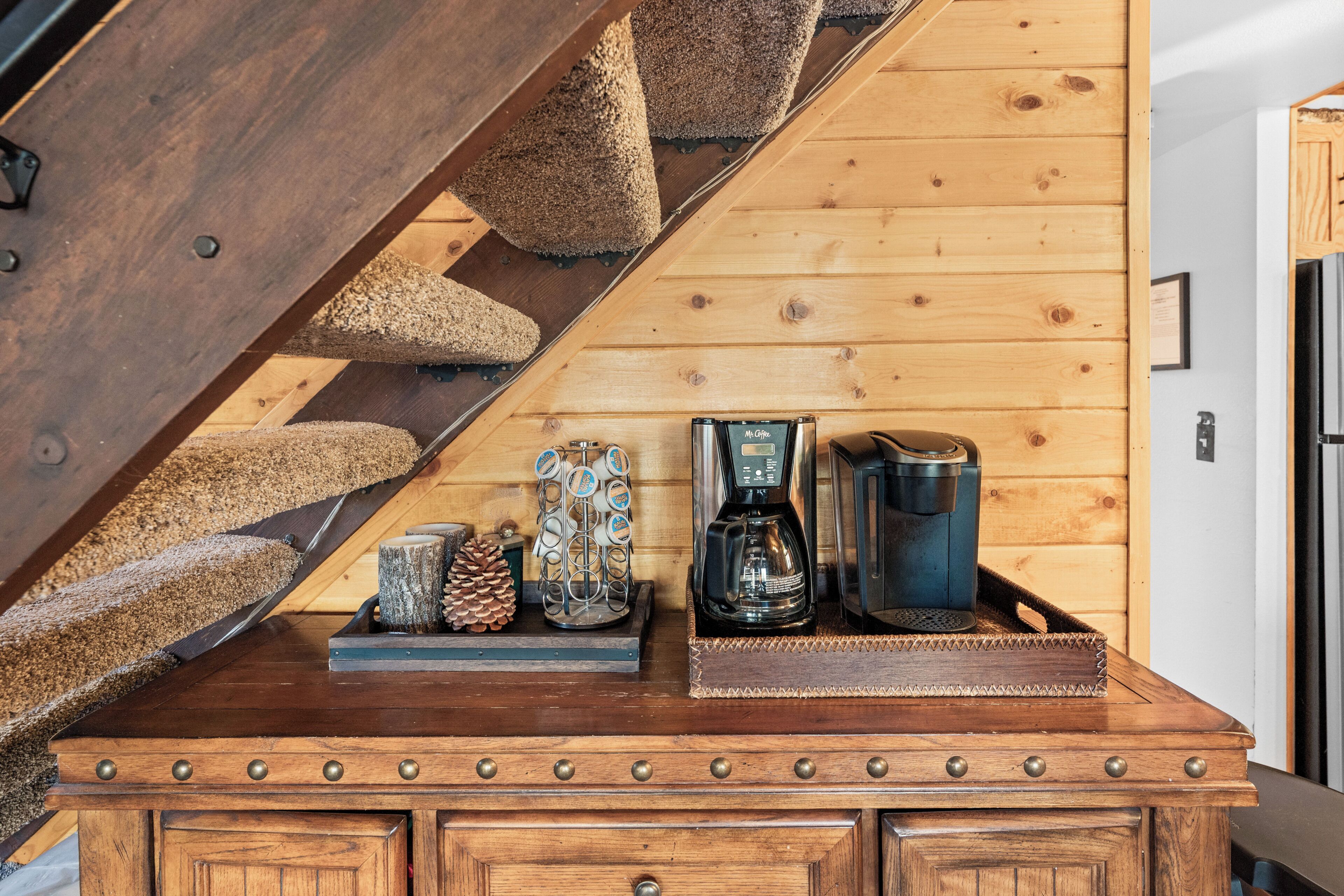 A wooden staircase with a metal handrail, leading to a wooden platform with a coffee maker, a thermos, and a decorative pine cone.
