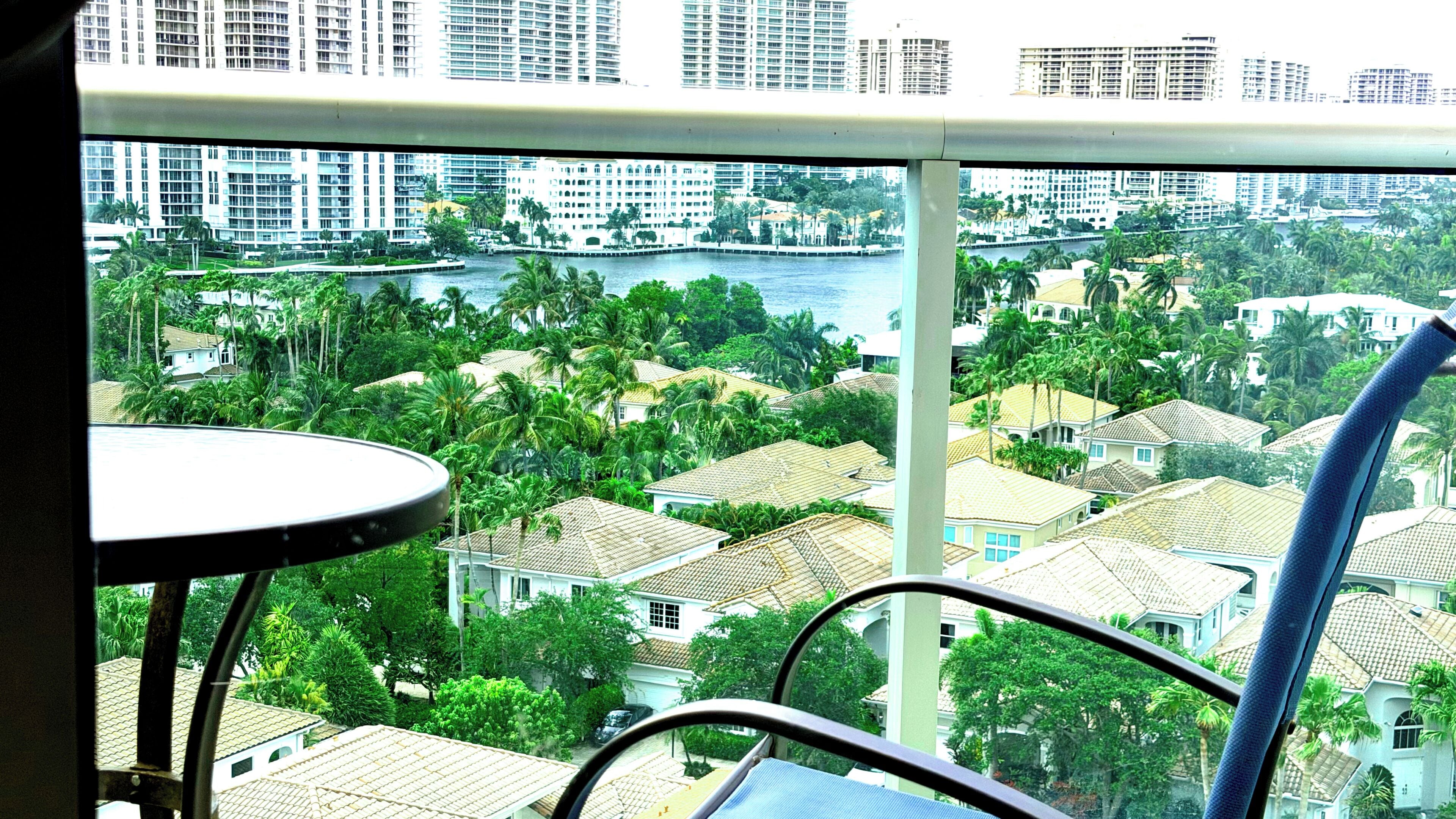 A balcony with a view of a river, palm trees, and residential buildings.