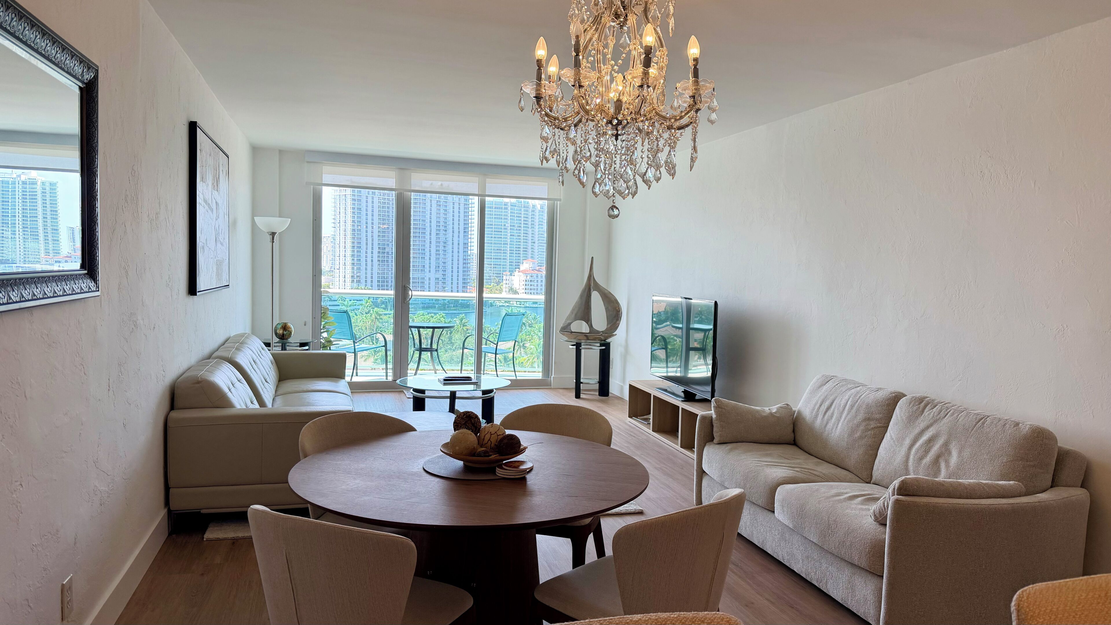 A modern living room with a chandelier, sofas, a dining table, and a television.
