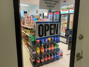 A store entrance with an 'OPEN' sign, shelves stocked with beverages, and a 7-Eleven visible in the background. - Lovely Condo with Intracoastal and Ocean Views! (Sunny Isles Beach)