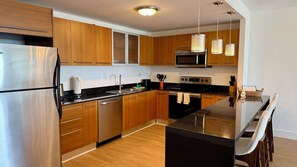 A modern kitchen with wooden cabinets, stainless steel appliances, and a black countertop. - Lovely Condo with Intracoastal and Ocean Views! (Sunny Isles Beach)