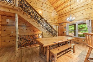 A wooden interior with a staircase, a dining table, and a window with a view of greenery. - Inspiration by Blue Creek Cabins (Cleveland)