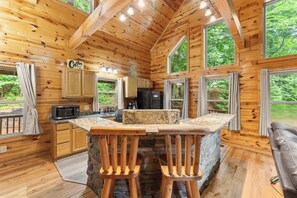 A wooden cabin interior with a kitchen, bar area, and large windows.