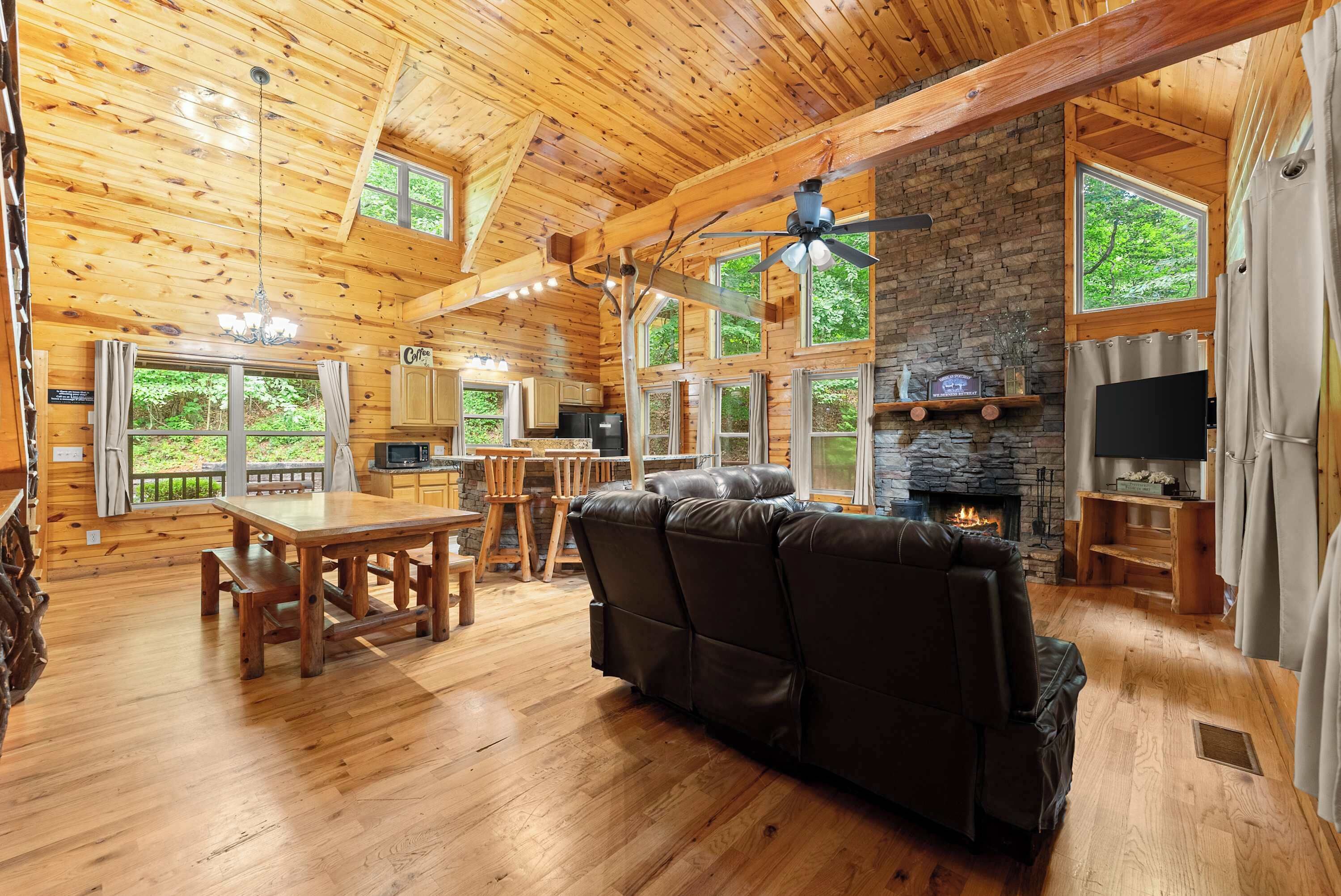 L’intérieur d’un chalet en bois comprend un coin repas, des sièges, une cheminée et de grandes fenêtres.