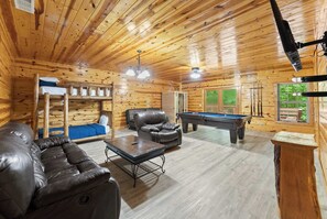 A wooden cabin interior with a pool table, leather sofa, bunk beds, and a ceiling fan. - Inspiration by Blue Creek Cabins (Cleveland)