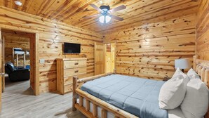 A wooden cabin interior with a bed, a television, and a ceiling fan. - Inspiration by Blue Creek Cabins (Cleveland)