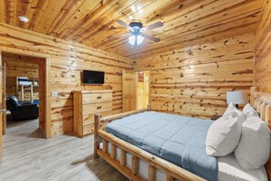 A wooden cabin interior with a bed, a television, and a ceiling fan. - Inspiration by Blue Creek Cabins (Cleveland)