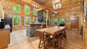 A log cabin interior with a dining area, kitchen, and large windows offering views of the outdoors. - Inspiration by Blue Creek Cabins (Cleveland)