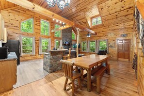 A log cabin interior with a dining area, kitchen, and large windows offering views of the outdoors. - Inspiration by Blue Creek Cabins (Cleveland)