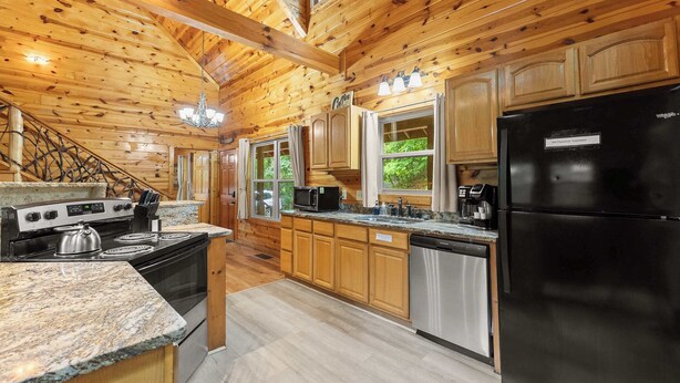 A modern kitchen with wooden walls, granite countertops, stainless steel appliances, and a chandelier. - Inspiration by Blue Creek Cabins (Cleveland)