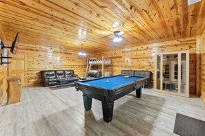 A wooden-paneled room with a pool table, leather sofas, and a ceiling fan.