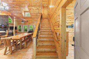A wooden staircase leading to a second floor, flanked by wooden walls and a dining area with benches and tables. - Inspiration by Blue Creek Cabins (Cleveland)