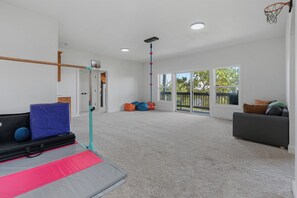 A spacious room with a basketball hoop, a padded floor, a sofa, and large windows offering a view of the outdoors. - Modern Family Retreat (Happy Valley)