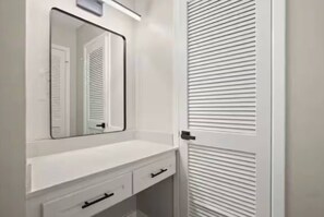 A white bathroom vanity with a mirror, a single drawer, and a door with horizontal louvered panels. - Central Austin • Parking • Sleeps 5 • Pet Friendly (Austin)