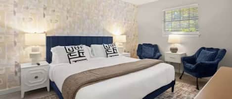 A hotel room with a bed, nightstands, a chair, and a window with blinds.