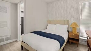 Ein Schlafzimmer mit Bett, Nachttisch und einem Fenster mit Jalousien.