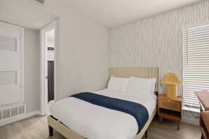 Ein Schlafzimmer mit Bett, Nachttisch und einem Fenster mit Jalousien.