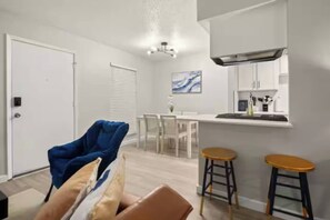 A modern kitchen with a built-in stove, a dining area with a table and chairs, and a seating area with a blue chair and two stools. - Central Austin • Parking • Sleeps 5 • Pet Friendly (Austin)